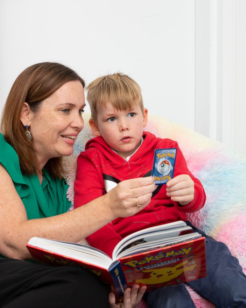child reading pokemon book with Let's Talk Let's Eat Speech Pathology Staff Member